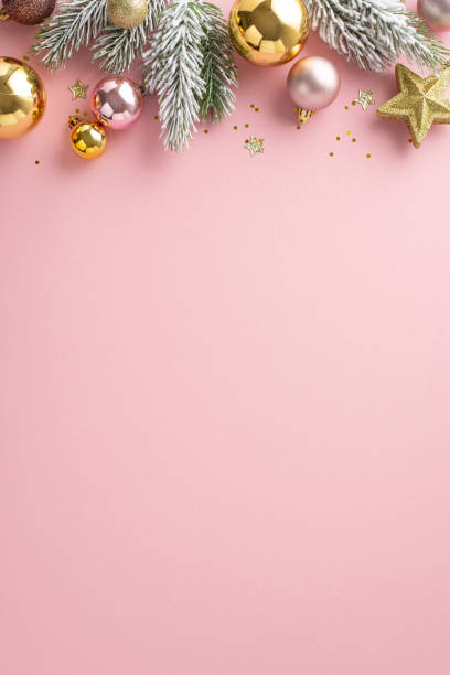 Sparkling New Year's Display: vertical top view of charming tree ornaments, shimmering star, pink and gold balls, sequins, pine twigs with frost on soft pink backdrop. Perfect for your holiday message