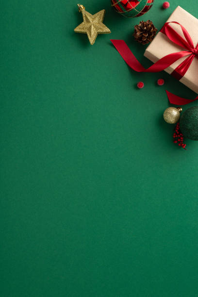 istock Seasonal Sparkle: Vertical top view of craft paper giftbox adorned with red ribbon bow, complemented by tree ornaments, shimmering golden baubles, ball, star, mistletoe berries on green backdrop 1719213034