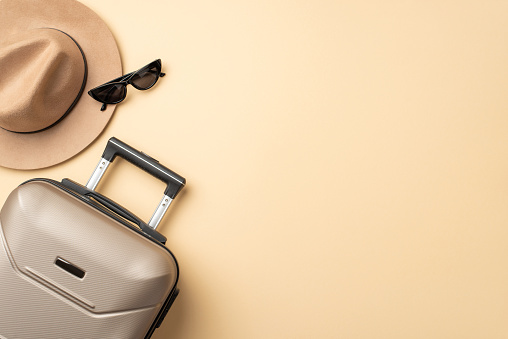 Sueños de viaje otoñales. Una toma aérea que muestra una maleta gris junto con un sombrero de fieltro ajustado y gafas de sol sobre un fondo beige aislado, ideal para sus necesidades promocionales o textuales photo