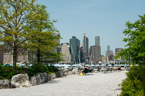 Brooklyn Heights, New York, USA, people relax on the Brooklyn waterfront, enjoying stunning views of the modern Manhattan cityscape in this captivating reportage photograph.