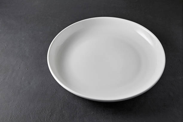istock White ceramic plate on a black stone table. Empty plate to display food in restaurant menu 1719217922