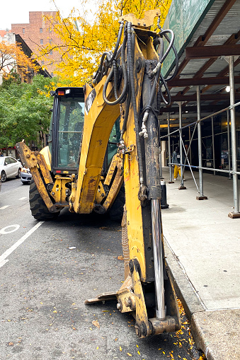 A line of heavy-duty construction vehicles, including a bright yellow bulldozer and an excavator, is parked on the bustling streets of Manhattan, New York City, USA.