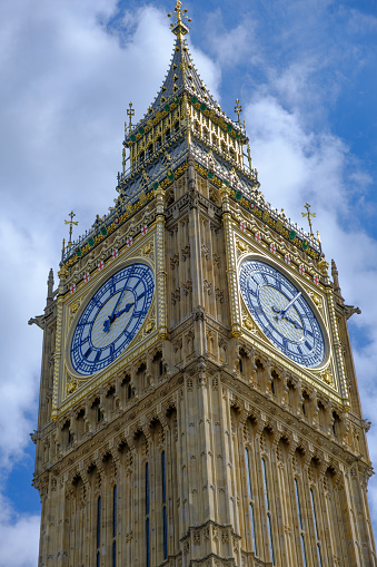 Big Ben clock set against partially cloudy blue sky. Landmark of London.