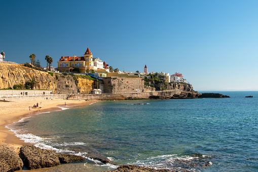 Cascais, Portugal: A picturesque rocky seashore with a stunning beach landscape, featuring panoramic views of the sea and a solitary palm tree.