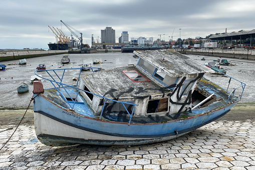 An old, weathered wooden boat sits abandoned on the shores of Lisbon, Portugal, overlooking the tranquil water.