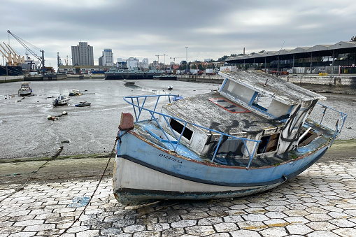 An old, weathered wooden boat sits abandoned on the shores of Lisbon, Portugal, overlooking the tranquil water.