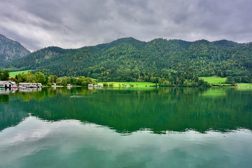 Lake Schliersee on a cloudy day. The Alps are reflected in the lake. Lake Schliersee is surrounded by greenery. Early autumn on Lake Schliersee.