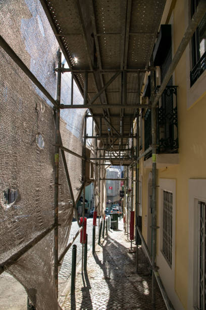 lisboa, portugal, reconstrução da fachada de um edifício de apartamentos histórico em uma rua da cidade, malha de construção de fachada cobre uma antiga casa fechada para renovação parede exterior - restoring house scaffolding history - fotografias e filmes do acervo