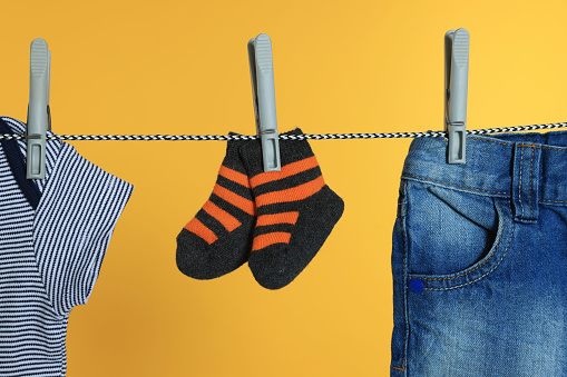 Different baby clothes drying on laundry line against orange background, closeup