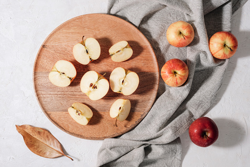 Fresh ripe apples on wooden tray with grey napkin and autumn leaves on white table. Autumn harvest, Thanksgiving concept. Top view, flat lay.