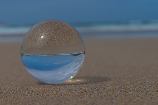 In the photograph you can see a crystal ball on the sand of the beach, in it you can see the sea, the waves and the sky.