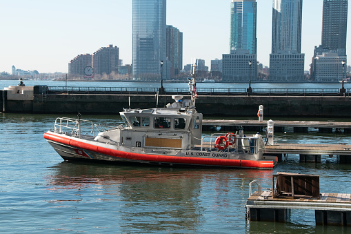 A Coast Guard boat is moored against a backdrop of sleek modern architecture in the Financial District of Manhattan, New York City, USA.