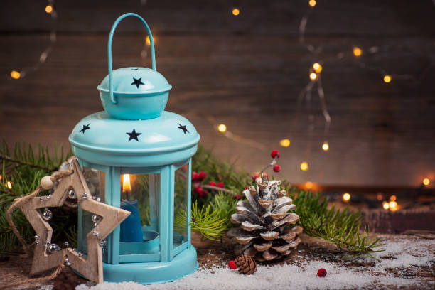 Candle in a holder with Christmas and New Year winter holidays symbols on a illuminated festive table with shiny lights