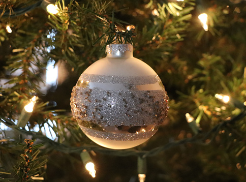 Traditional sparkling, silver Christmas ball hanging on illuminated tree.