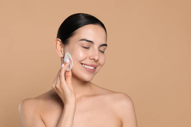 istock Young woman using cotton pad with micellar water on beige background, space for text 1719330224