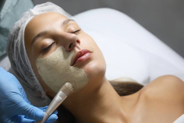 istock Cosmetologist applying mask on client's face in spa salon 1719355367