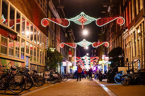 In Amsterdam, Netherlands the city is illuminated with seasonal decorative lights on a winter night  in a pedestrian zone where people can be seen in the distance.