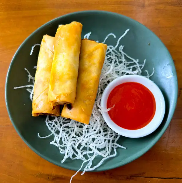 Close Up Fried Spring Rolls or Lumpia Served in restaurants with chili sauce and fried vermicelli on a green plate