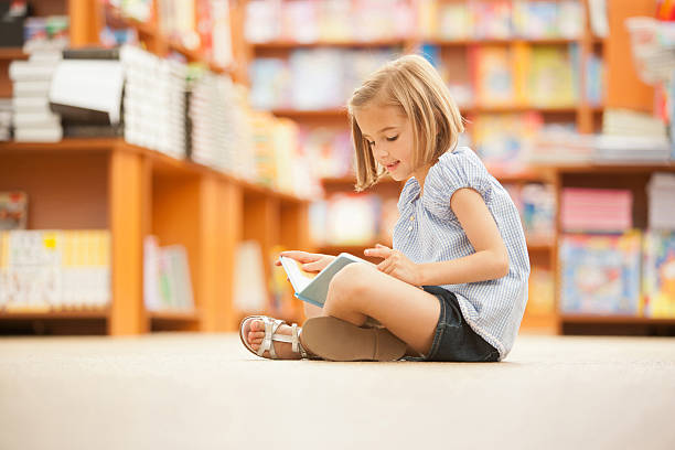 mädchen auf dem boden sitzen auf bibliothek mit einem buch - child reading education book stock-fotos und bilder