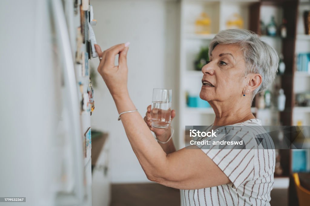Senior woman checking medical prescription on refrigerator door Refrigerator Stock Photo