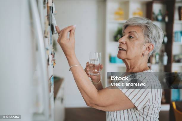 Senior Woman Checking Medical Prescription On Refrigerator Door Stock Photo - Download Image Now