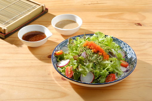 A fresh and flavorful Japanese shrimp salad is served on a wooden table, drizzled with a delicious soy-sesame dressing.
