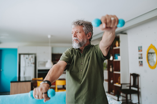 Elderly man exercising at home with dumbbell physiotherapy