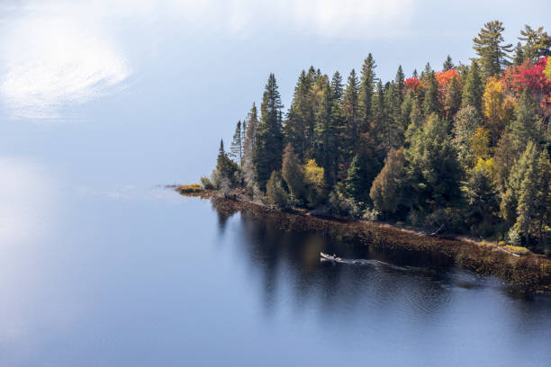 A boat cuts through the reflections of the Autumn coloured trees, as seen from the top of Centennial Ridges Trail in Algonquin Park, Muskoka, Ontario, Canada.