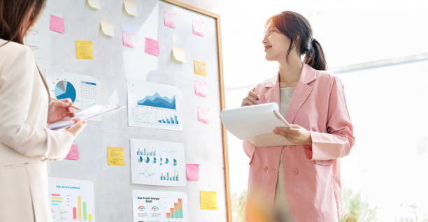istock Working together on project. Two young business female colleagues working on document and business growth graph on white board, standing in office. 1719643789