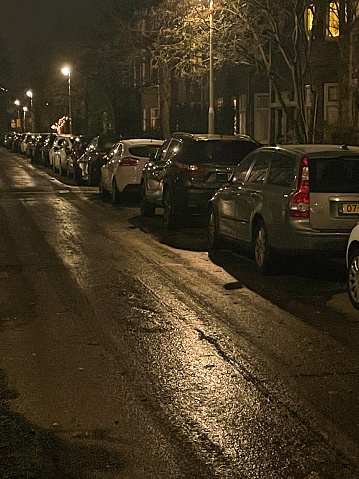 den haag, netherlands - december 18 2022: almost invisible black ice is covering the small street with parked cars