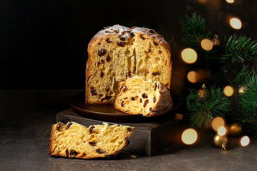 Panettone, Italian Christmas cake with raisins and candied fruits  on wooden plate with Christmas tree branch and gold decoration.