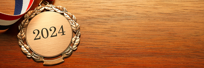 Gold medal engraved with the year 2024 rests on a wood desk.