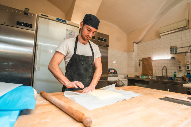 istock Caucasian Male Baker Using A Rolling Pin On A Counter In An Artisan Bakery 1719690307