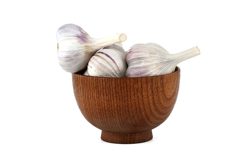 Freshly harvested garlic bulbs in wooden bowl isolated on white background