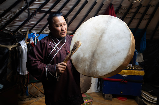 Ulaanbaatar, Mongolia - October 3, 2023: A shaman holds up a drum used during a seance at his shrine inside a ger (yurt).