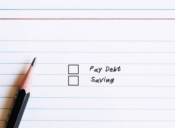 istock Paper notebook sheet and a pencil , with two choices checklists to choose between DEBT and SAVING. Concept of financial decision making 1719759362