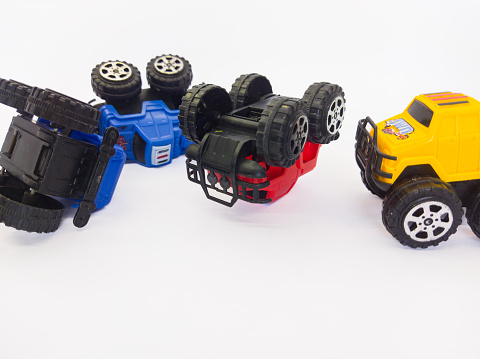 A collection of off-road toy cars made of plastic rolled over a white background, there are blue, red and yellow cars