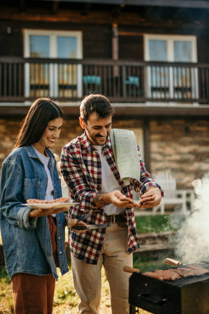 istock Two people share a delightful BBQ experience, with the grill master expertly flipping meat while his partner adds a flavorful touch. 1719906397