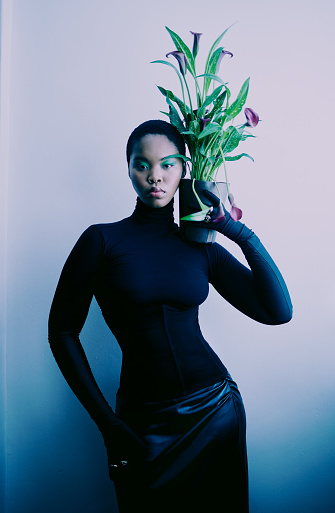 A fashion photo of a beautiful African model posing whist holding a plant on her shoulder