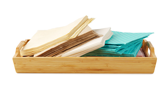 Heap of paper napkins on wooden tray on white background close up