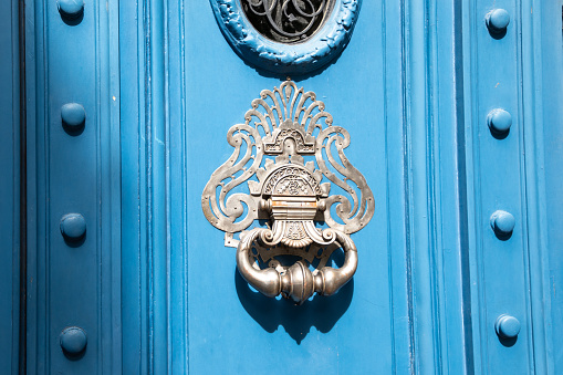Old iron ring chrome silver knocker on vintage wooden retro blue door for knocking on facade classical europe house