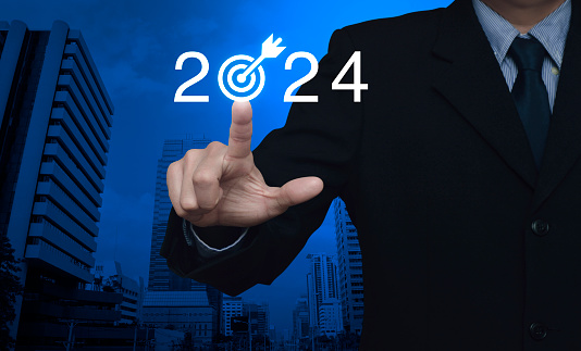 Businessman pressing 2024 letter with goal icon over modern office city tower and skyscraper, Business happy new year 2024 success concept