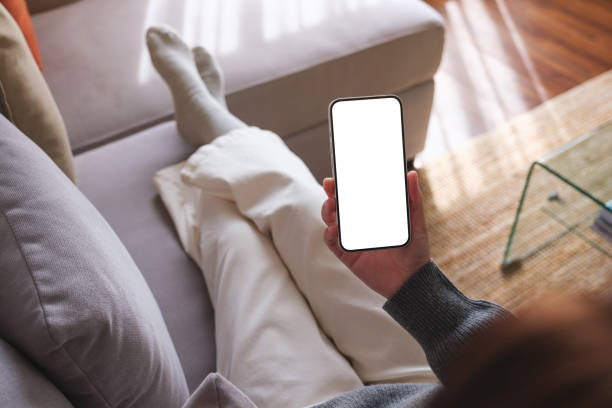 istock Top view mockup image of a woman holding mobile phone with blank desktop white screen while lying on a sofa at home 1720018505