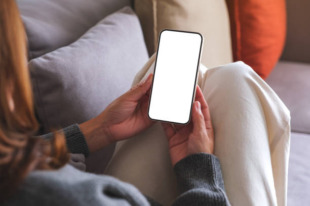 istock Mockup image of a woman holding mobile phone with blank desktop white screen while lying on a sofa at home 1720019034