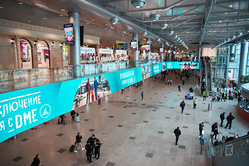 A snapshot of the fast-paced life of airport travel, with business travelers walking past with their rolling luggage or waiting for their flight. In the background, a recently landed airplane can be seen through the glass window.