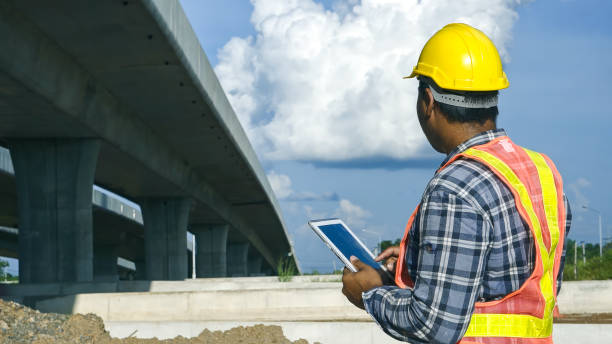 istock Asian foreman using tablet to record electronic data on construction site of concrete highway bridge. Inspection project road construction development. 1720038715
