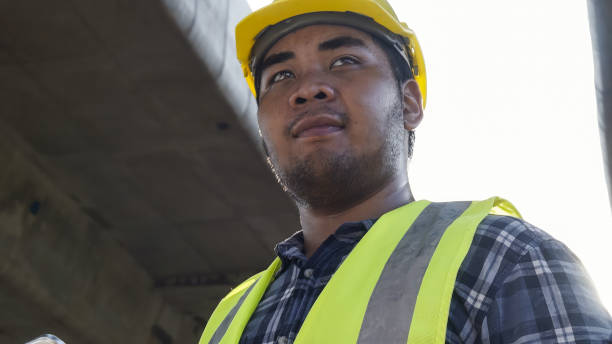 istock Close up face Asian foreman check work on construction site of concrete highway bridge. Inspection project road construction development. 1720038747