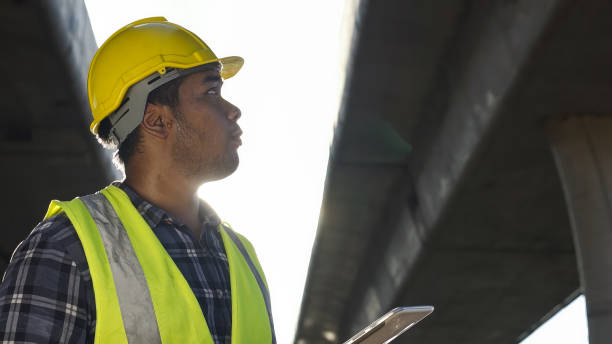 istock Asian foreman using tablet to record electronic data on construction site of concrete highway bridge. Inspection project road construction development. 1720039291