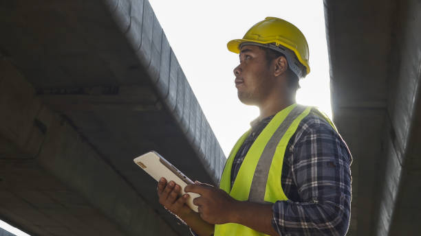 istock Asian foreman using tablet to record electronic data on construction site of concrete highway bridge. Inspection project road construction development. 1720039895