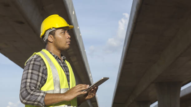 istock Asian foreman using tablet to record electronic data on construction site of concrete highway bridge. Inspection project road construction development. 1720040712